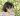 photo of a brown nonbinary person looking.off camera in front of green foliage. they. have glasses, shouldere length black hair, and. a blue and pink striped shirt and matching necklace