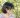 photo of a brown nonbinary person looking.off camera in front of green foliage. they. have glasses, shouldere length black hair, and. a blue and pink striped shirt and matching necklace