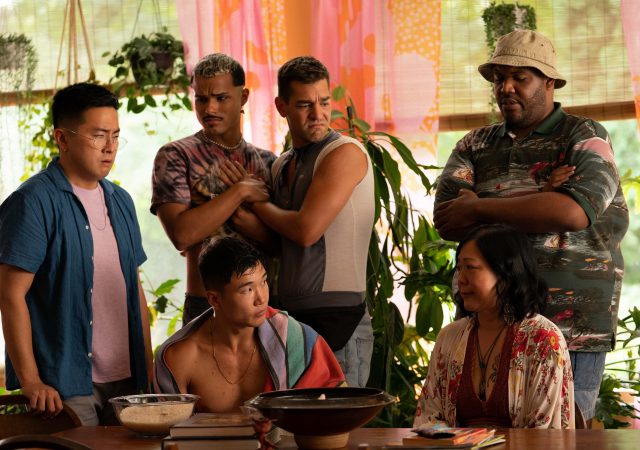 still from Fire Island (2022) depicting the main group of characters looking sad and concerns around a dining table