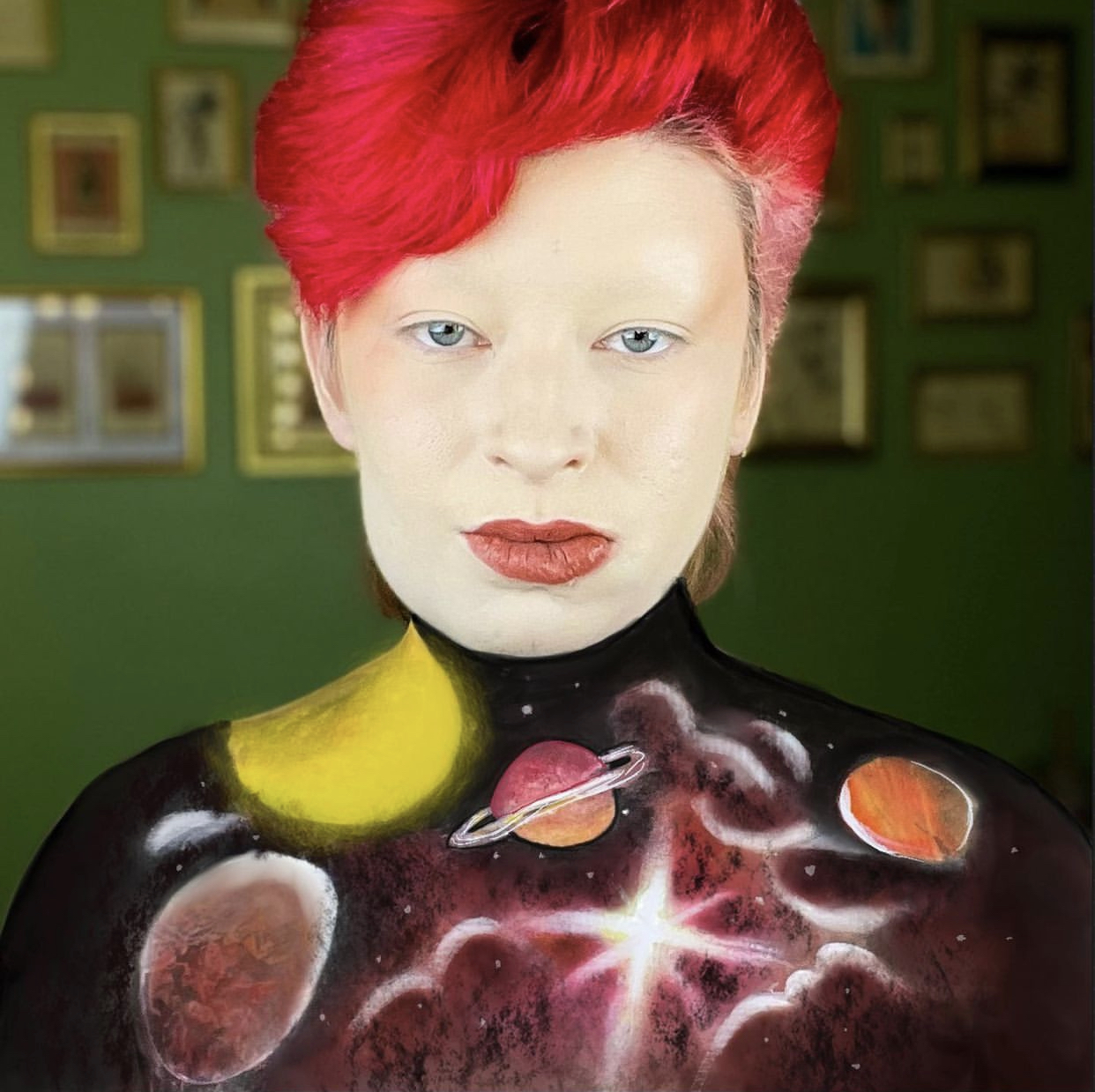 photo of The Mother Birdie, a white nonbinary person with short, bright red hair, bold red lips, and their chest painted with realistic planets and stars
