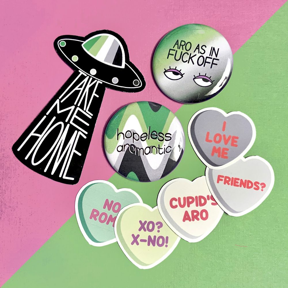 photo of stickers and buttons themed around aromantic pride on a split pink and green background.