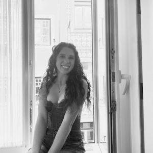 Black and white photo of Taylor, a smiling white woman with long dark wavy hair, a tank top, and a pendant necklace.
