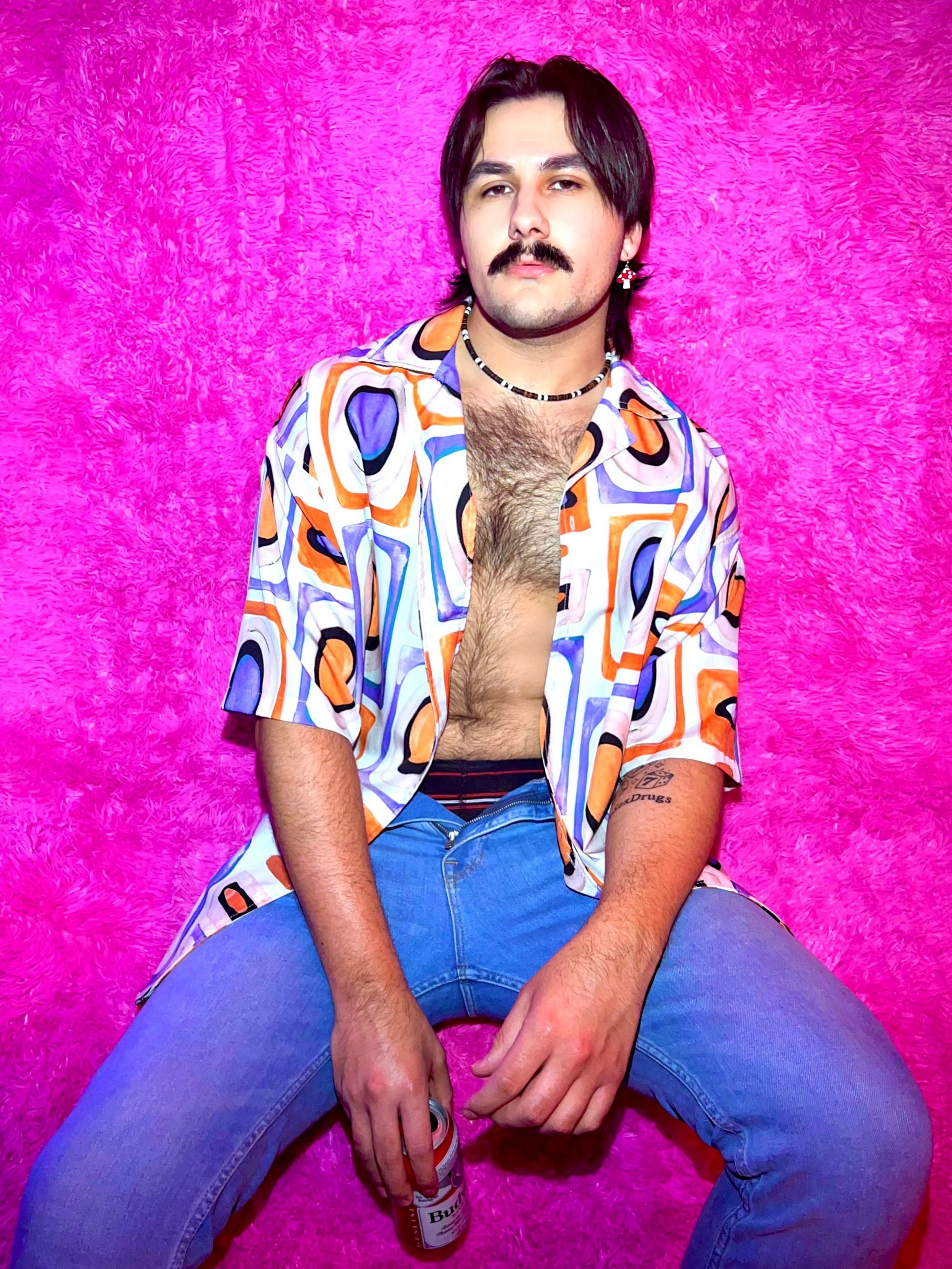 photo of Michael Medrano, a white man with shoulder length brown hair, a mustache, and a patterned shirt open over a hairy chest
