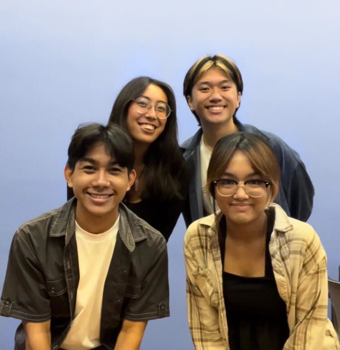 A photograph of Kabalikat Kore members against a blue wall. From left to right, top to bottom: a femme person with brown skin and long black hair wearing round glasses, a masc person with brown skin and blonde and black hair wearing a dark blue shirt, a masc person with brown skin and short black hair wearing a dark gray shirt, and a femme person with brown skin and dyed brown hair wearing glasses and a light flannel.