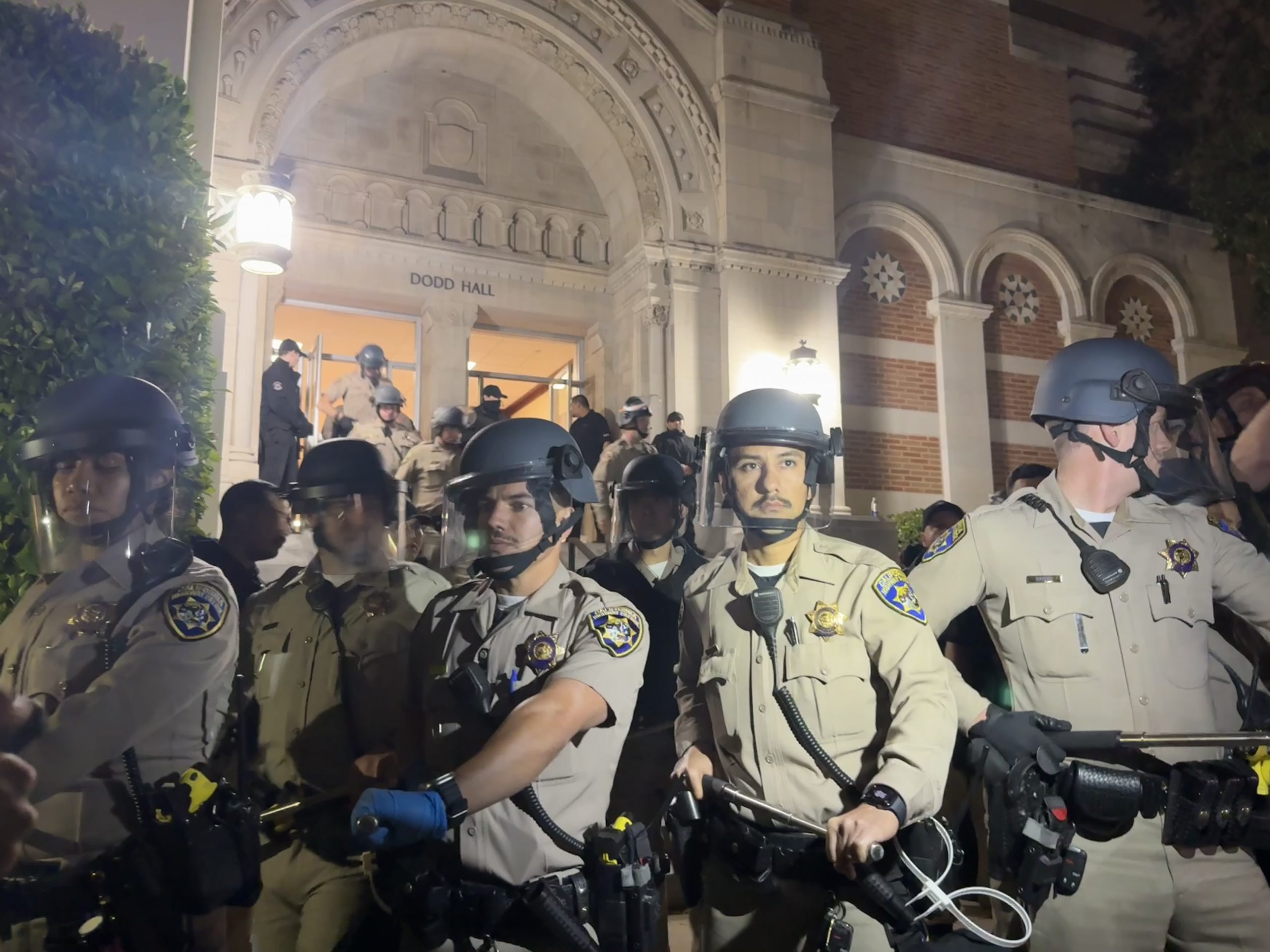 A crowd of police officers wearing face shields and wielding truncheons stand outside Dodd Hall on the night of May 1, 2024.
