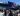 A crowd of anti-RIMPAC protestors with banners and flags gather in front of a U.S. Navy aircraft carrier.